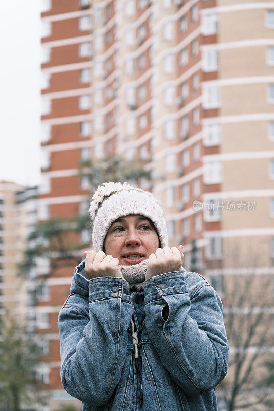 在寒冷的城市街道上，一名妇女正冻得双手发热