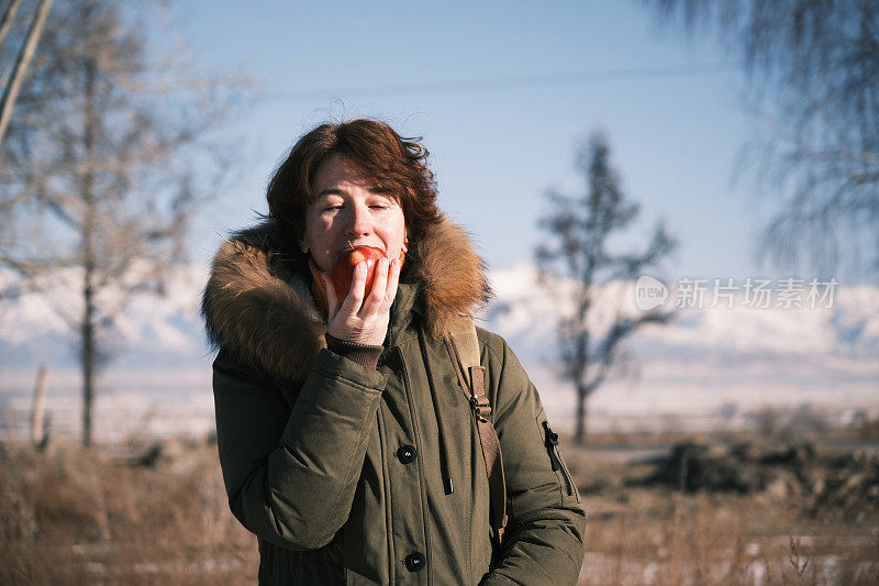 一个走在冬天路上的女人打算吃一个苹果