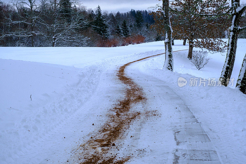 滑溜的冬季道路，人行道上的公园，覆盖着冰和撒着沙。防滑，冰上安全。冬季美丽的公园景观