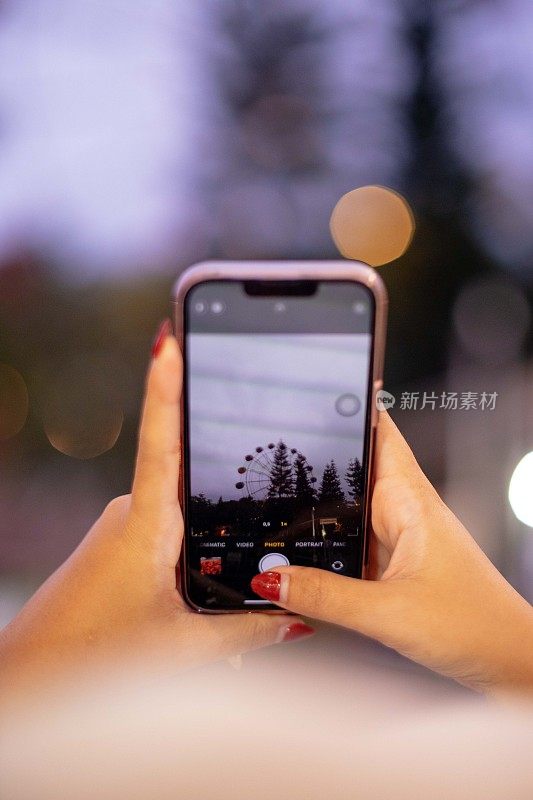 亚洲女孩在黎明时分手持手机拍摄摩天轮的特写镜头