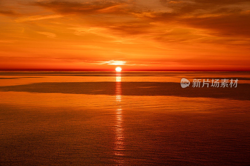 明亮的橙色日落在海上。云和地平线在海上相接。