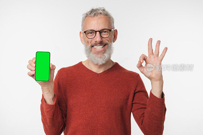 微笑快乐的高加索成熟中年男子拿着手机，智能手机的模拟屏幕显示了白色背景中孤立的手势