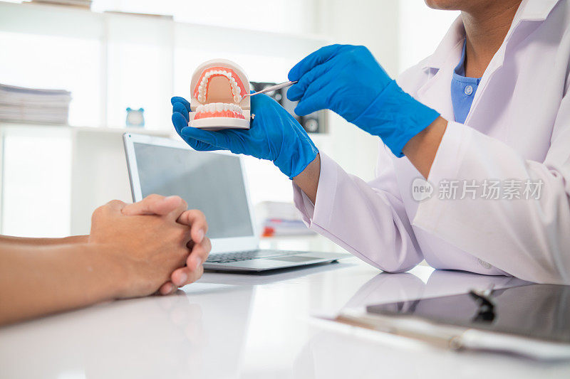 牙医手里拿着假牙，向病人展示问题牙齿的位置，并向病人解释如何治疗牙齿，以便病人理解。文本复制空间