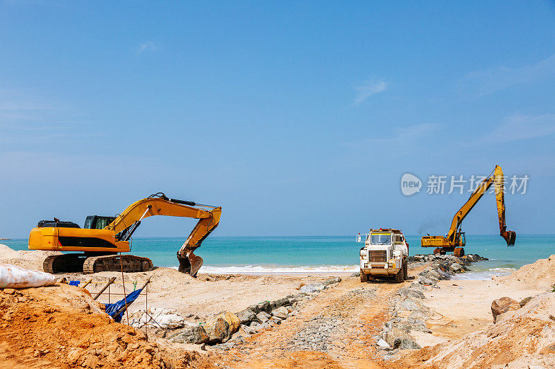 沿海建设:黄色挖掘机和卡车在海滨建筑工地。