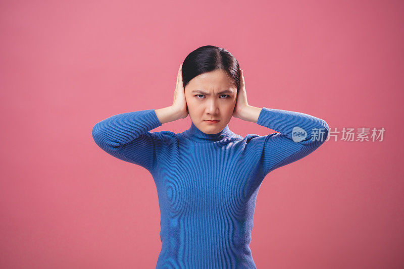 亚洲女人愤怒地看着镜头，孤立在粉红色的背景上。