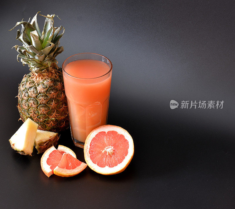 在黑色背景上混合了热带水果的鲜榨果汁，旁边是半熟的葡萄柚和菠萝。