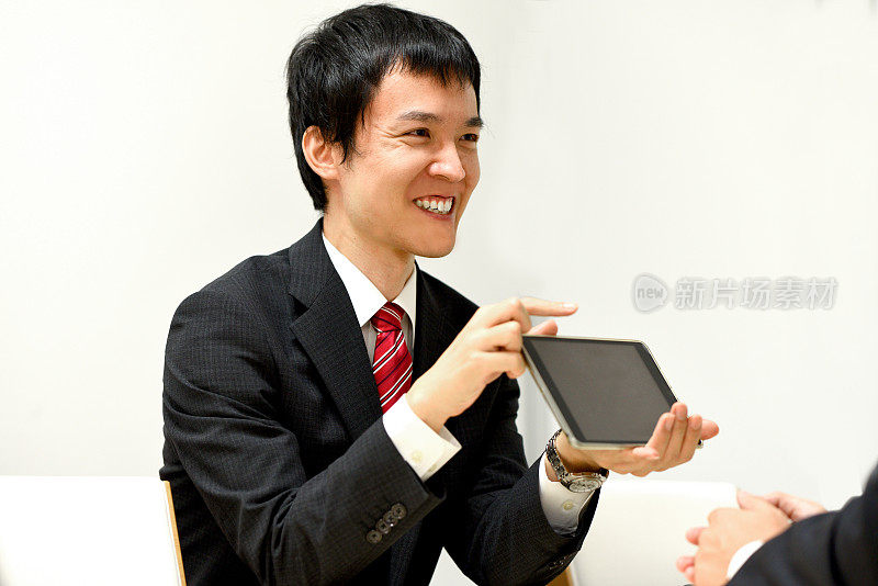一位穿着西装的年轻亚洲男子在平板电脑终端上解释