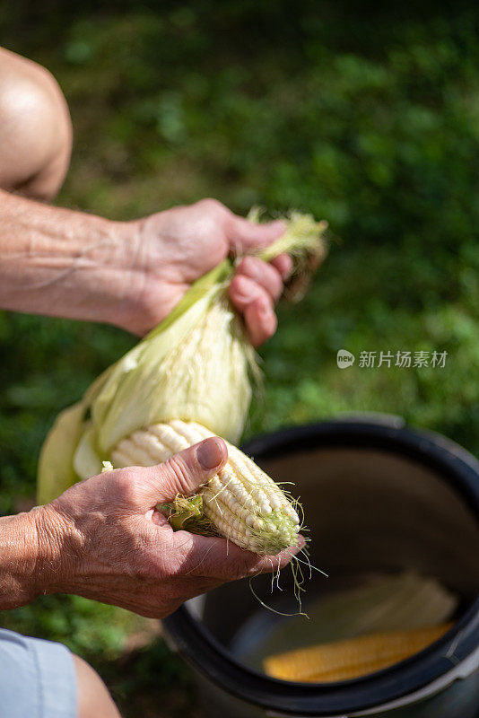 一名男子在室外的院子里剥新鲜的甜玉米