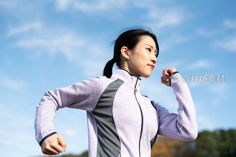 年轻女子在蓝天下的秋天公园慢跑的特写