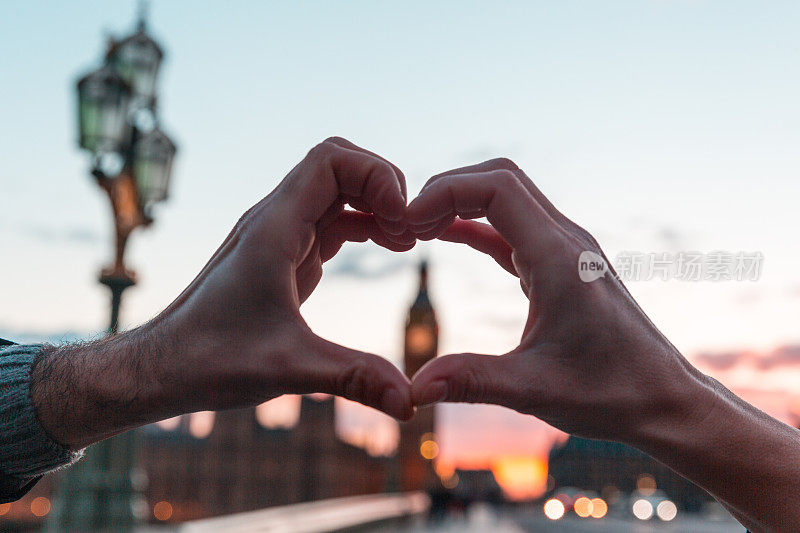 一对夫妇在伦敦用手做一个心形，背景是大本钟