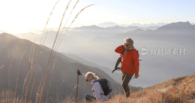 一对成熟的夫妇早晨沿着长满草的山坡徒步旅行