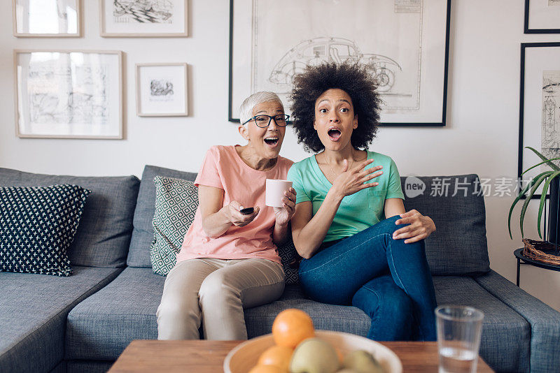 老年妇女和她年轻的邻居在看一些令人兴奋的电视节目
