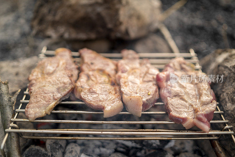 制作两片猪肉或牛肉的过程。肉烤在金属便携式烧烤烧烤架与明亮的火焰和余烬木炭