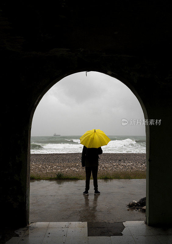 一个孤独的男人撑着伞在一个下雨的早晨站在海滩上