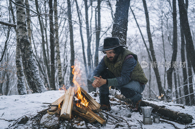 年轻人在清晨雪山森林的篝火旁享受咖啡