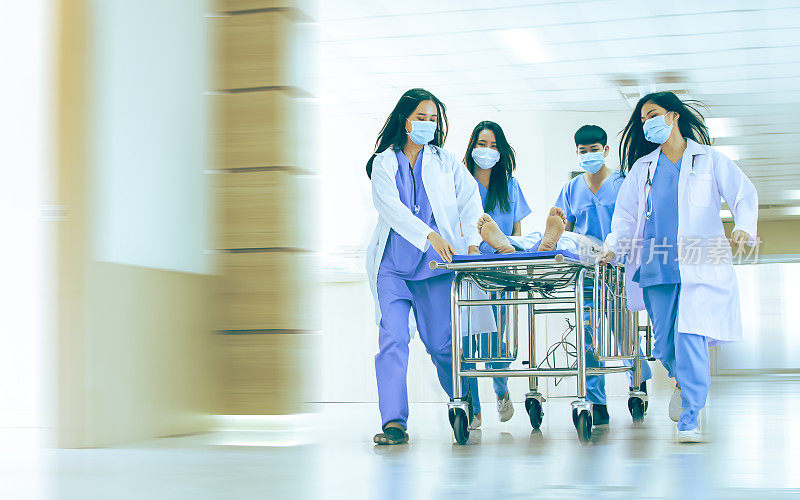 亚洲专业团队合作的医生、护士，身穿手术服和白大褂制服，在医院走廊的病床上匆忙地救治意外重伤的急诊病人。
