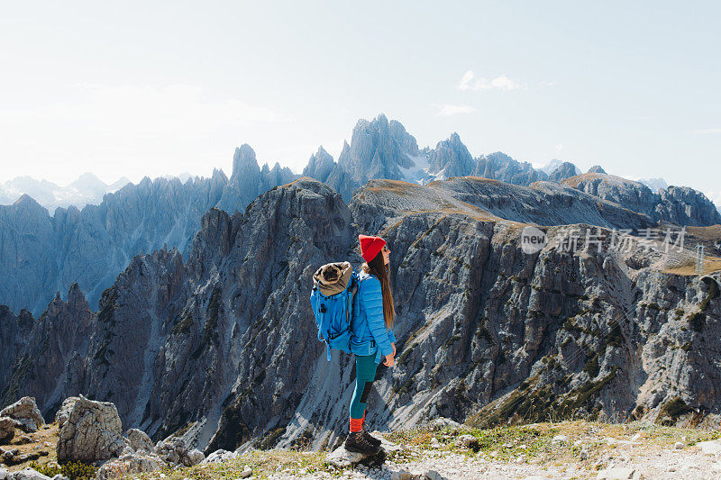 年轻女子抱着狗在背包里凝视风景优美的山脉徒步旅行在白云石阿尔卑斯山