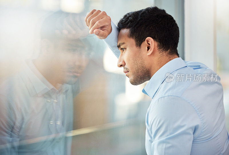 一个年轻的商人靠在窗户上，看起来很沮丧