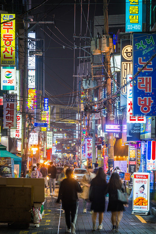 首尔繁忙的街道上熙熙攘攘的人群，霓虹灯照亮了韩国的夜景