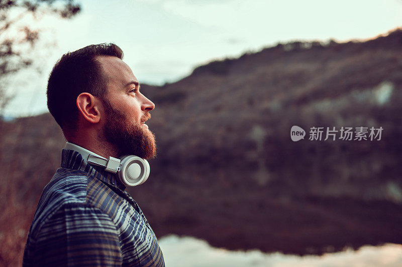 戴着耳机的大胡子男人一边停下音乐欣赏大自然，一边对未来感到乐观
