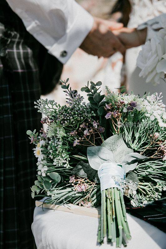 垂直拍摄的新娘和新郎手牵手，前景中有一束花