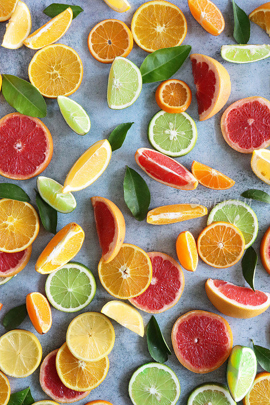 柑橘水果切片和叶片楔形全帧图像，血橙，塞维利亚橙，柠檬和酸橙的横截面，斑驳的灰色背景，提高的观点