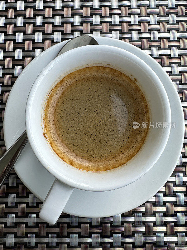 特写图像:白色杯子和茶托里新倒的黑咖啡，金属和玻璃咖啡桌上放着两块饼干，咖啡馆里的热饮，关注前景