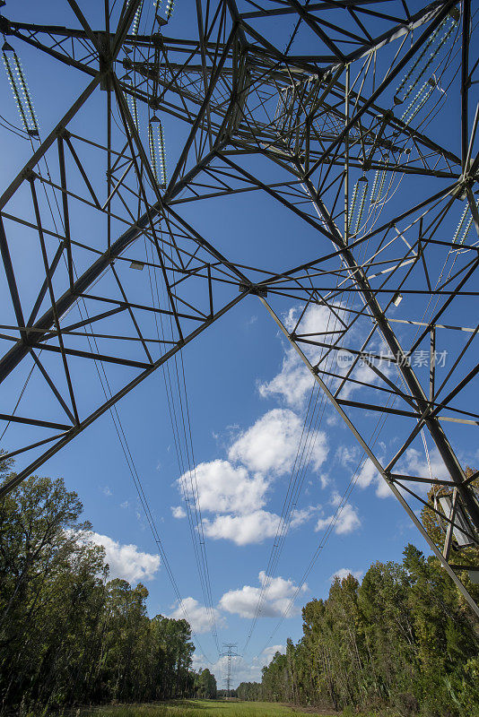 从电力塔下拍摄的广角镜头，电缆通向遥远的森林里的电力塔，蓝天下点缀着片片白云