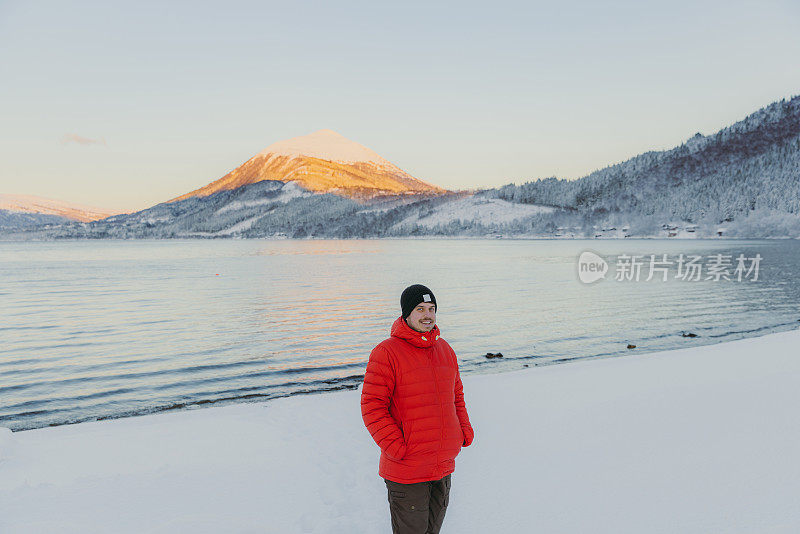 微笑的男人在挪威的日落时分，在湖边散步，欣赏风景秀丽的雪山
