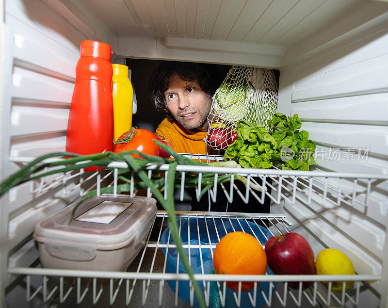 一个人把蔬菜放进冰箱，可持续发展的概念