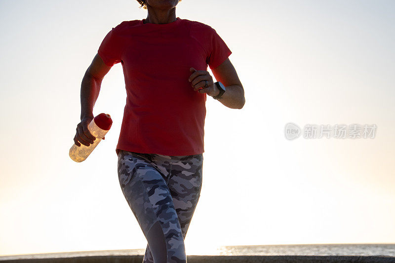 健康的女人慢跑与一个水瓶在日落