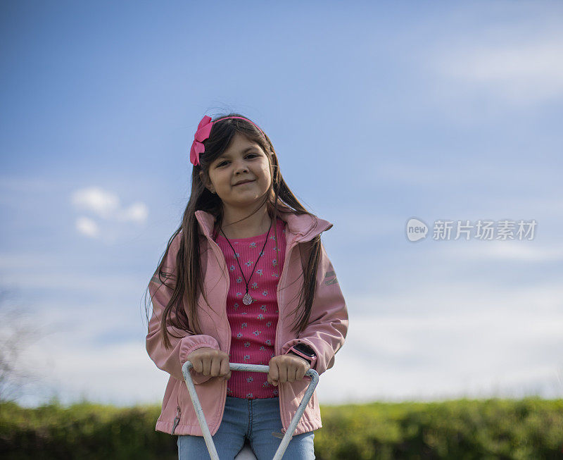 可爱的小女孩正在公园里玩跷跷板。现在是春天。