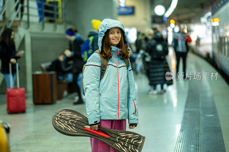 一个十几岁的女孩拿着滑板在火车站等火车。
