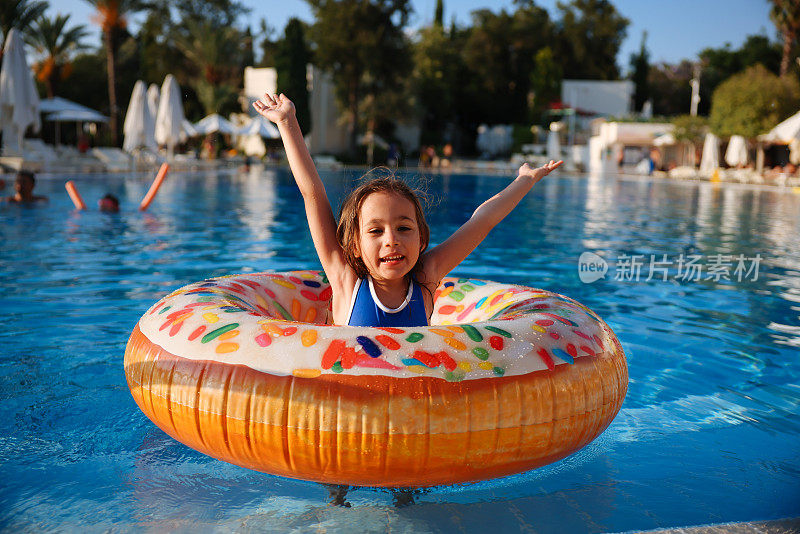 可爱有趣的十几岁的女孩穿着泳装，带着甜甜圈救生圈在游泳池里游泳