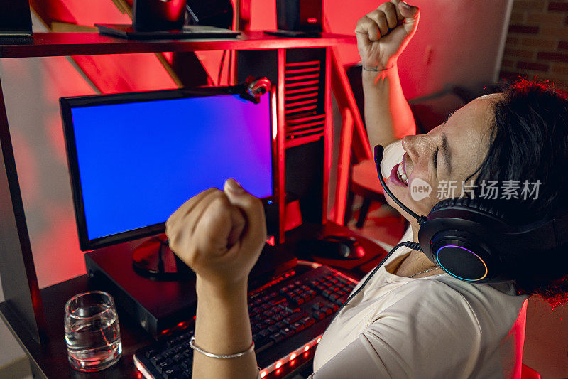 兴奋的拉丁玩家戴着耳机在家里玩在线视频游戏。