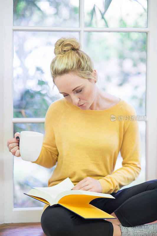 年轻貌美的白人女子坐在窗边看书喝茶