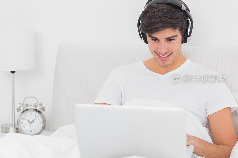 快乐的人坐在床上用笔记本电脑听音乐