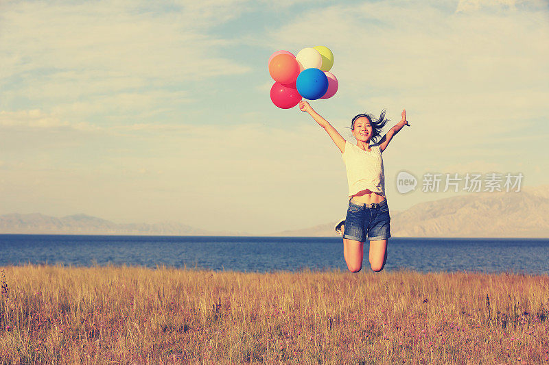 欢呼年轻女子在日落的草原上跳跃彩色气球