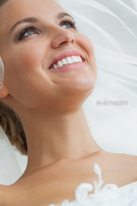 微笑浪漫的年轻新娘戴着面纱摆姿势看别处