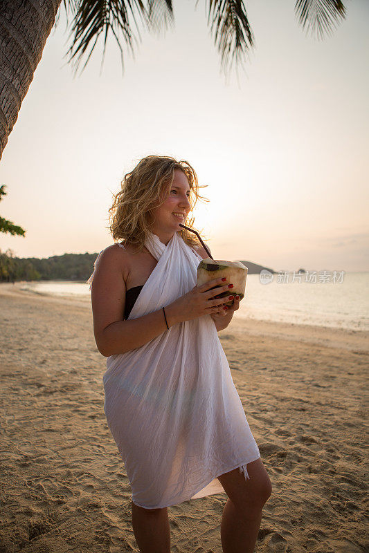 快乐的年轻女子在热带海滩喝椰子日落