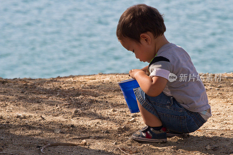 蹒跚学步的孩子在湖边玩沙子和石头