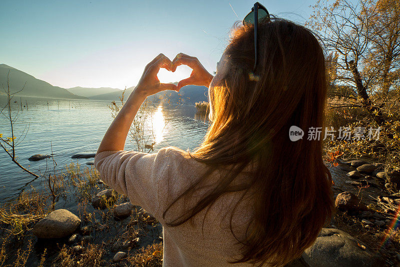 年轻女子在湖边做心形手指架