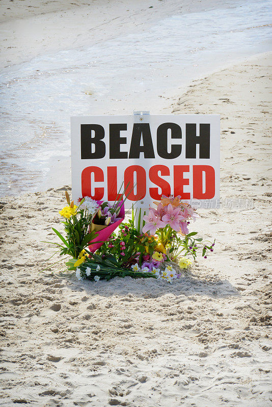 “海滩关闭”的牌子上放着鲜花，表示死者已经死亡