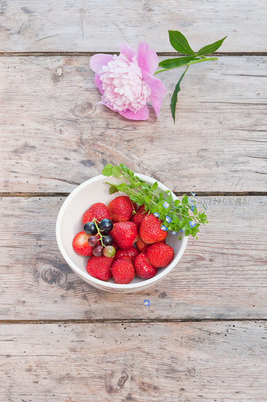 木桌上放着草莓、覆盆子和牡丹