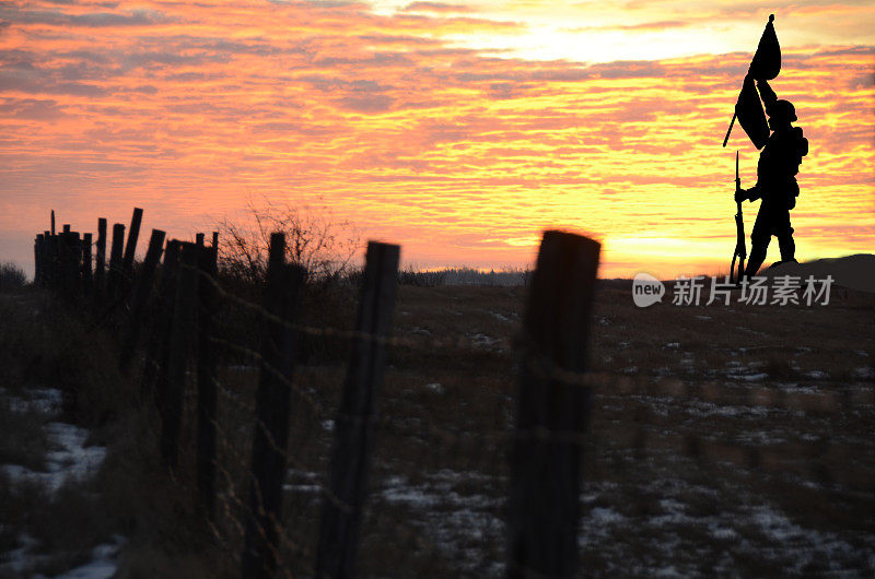 日落时，手持旗帜的士兵剪影穿过田野