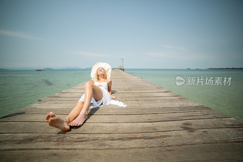 在热带海滩的木制码头上晒太阳的女人