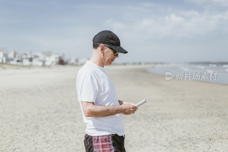 一个在海滩上看手机的成熟男人的肖像