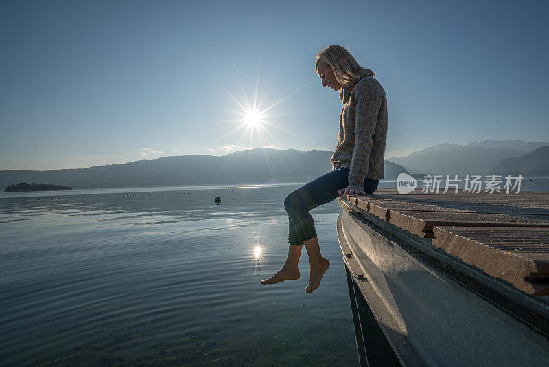 年轻女子在湖边码头休息，看日落