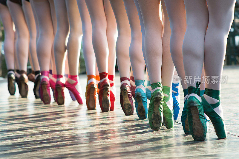 在一场表演中，芭蕾舞者的脚穿着几种颜色的芭蕾舞鞋在舞台上跳舞。