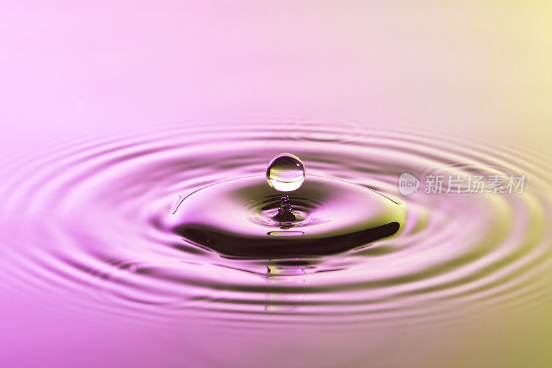 水滴近距离与同心涟漪在鲜艳的粉红色和黄色表面